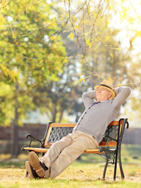 Elderly gentleman sitting on a bench in park on a sunny day